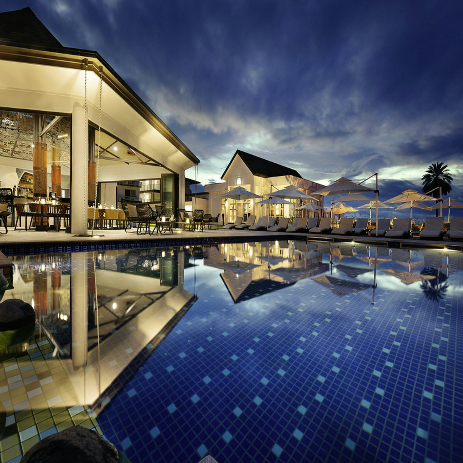A beachfront vacation rental villa with a pool lit at dusk.