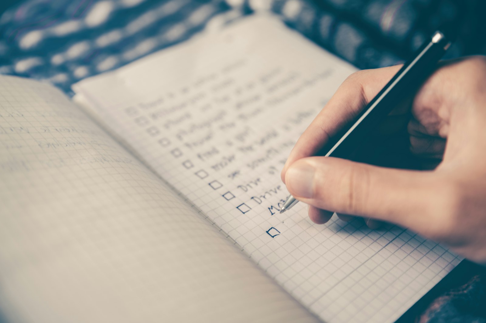 An open notebook with a handwritten checklist next to a laptop and coffee cup.